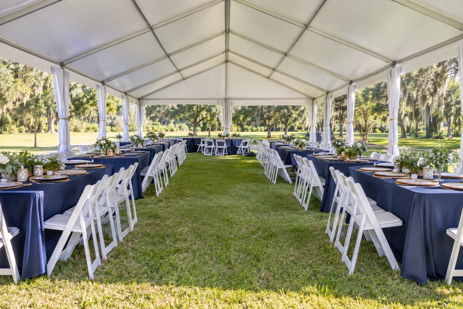Community feast under large rectangular tent, rows of navy linen banquet tables and white resin chairs, wide central walkway, grassy field with oaks, bright morning