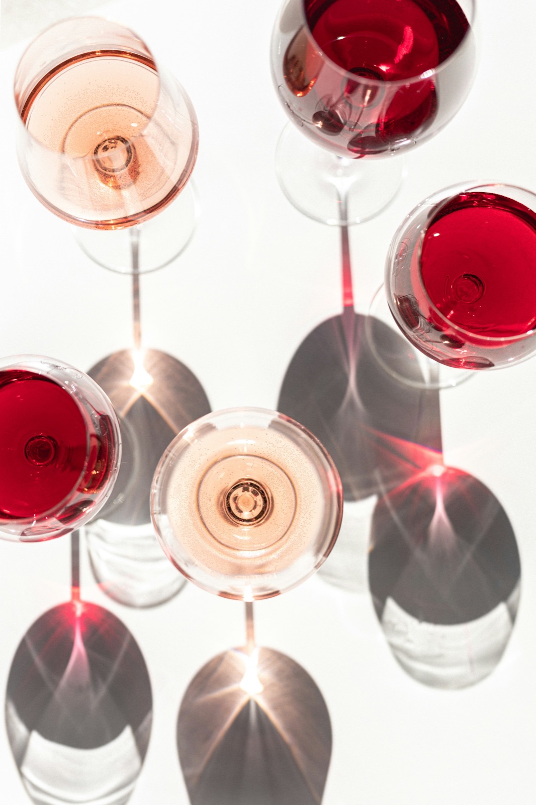 Overhead red and rose wine glasses casting shadows in sunlight.